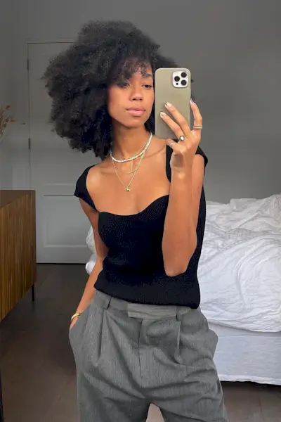 outfits to wear on a first date shown on a woman wearing a black top with relaxed trousers and layered chain necklaces