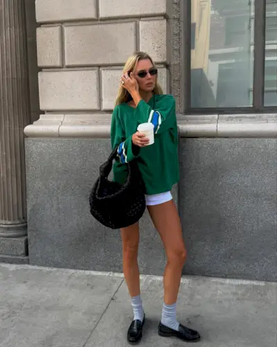 woman wearing white shorts and oversized long sleeve green shirt and loafers