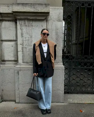 Mary wears a brown sweater, black blazer, jeans, white tank top, black handbag, and black loafers.