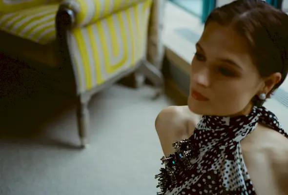 Actress Louisa Jacobson wears a scarf-print Dries Van Noten halter dress with Sauer jewels. She is posing for portraits inside her hotel room before The Gilded Age season 3 premiere.
