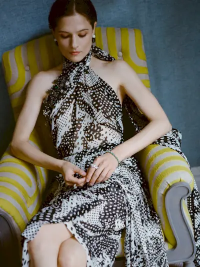 Actress Louisa Jacobson wears a scarf-print Dries Van Noten halter dress with Sauer jewels. She is posing for portraits inside her hotel room before The Gilded Age season 3 premiere.