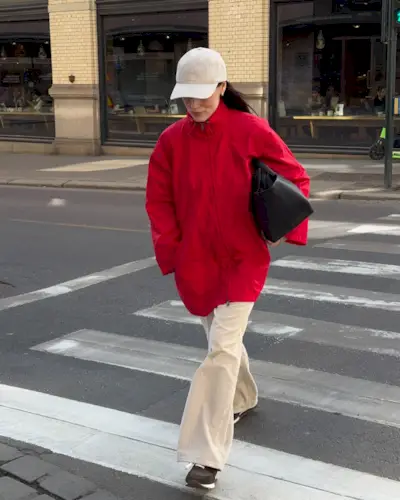 Influencer @annabelrosendahl crosses the street wearing a red jacket with cream trousers and brown trainers.