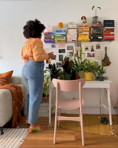 A woman wears an orange sweater, blue straight-leg jeans, and tie-dye heels.