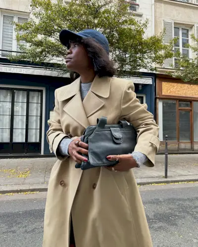 woman wearing a camel coat, black bag and baseball cap