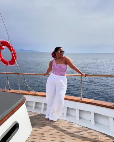 Karina in a light pink and dark pink one shoulder swimsuit, white linen trousers and hot pink and blue scrunchie.