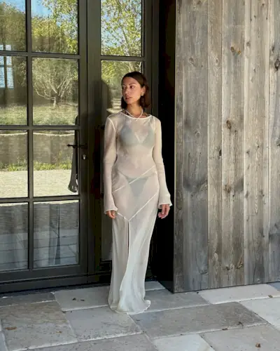 Marianne Smyth in a dark brown bikini and sheer ecru cover up on a wooden background.
