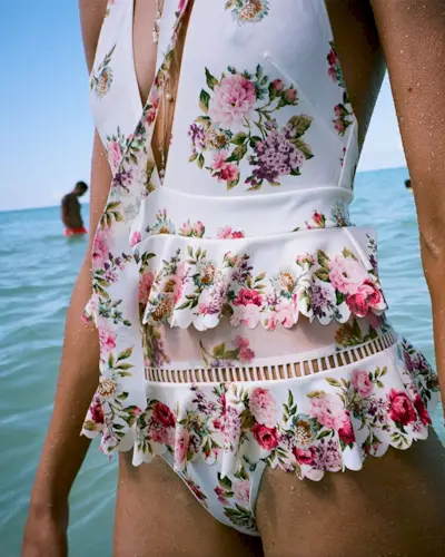 a model wears a white floral one-piece swimsuit with two tiers of ruffles