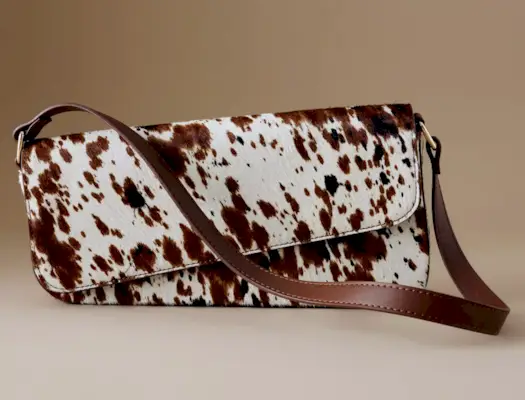 Influencer in brown jacket cream trousers, white scrunchie and a cow print hobo bag.