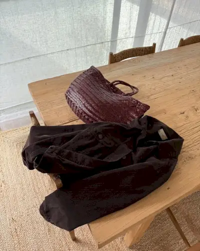 @monikh shares her burgundy woven leather basket bag as it lies on a wooden table