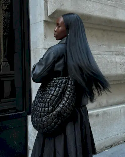 Woman wears leather jacket, black crossbody bag and black skirt