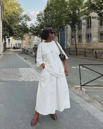 French fashion influencer Frann Fyne wearing a white T-shirt and maxi skirt with ballet flats and a pendant necklace.