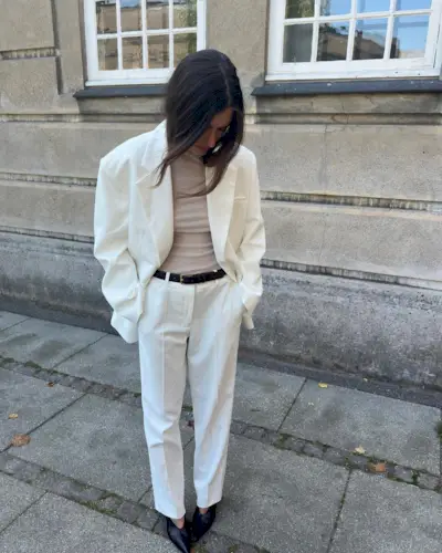 Fashion influencer Lida Krasniqi wearing a white pantsuit, black belt, and sheer turtleneck.