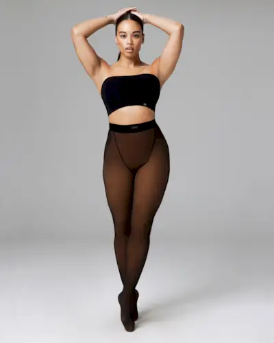 Woman wearing a red quilted jacket and matching skirt, nude-colored fleece-lined tights, and heels and standing in front of brick building.