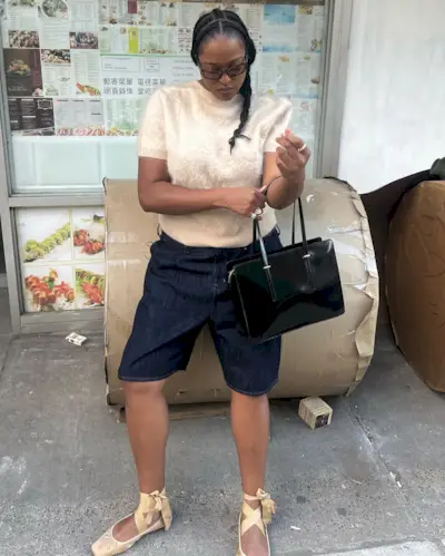 Imani wearing a J.Crew cashmere shirt, denim Bermuda shorts, and espadrille sandals.
