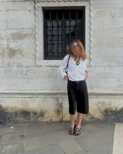 Silvia wearing a white button down, black Bermuda shorts, and mesh flats in front of a marble building.