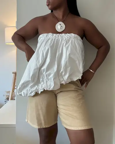 Nnenna wearing a strapless white bubble top, tan Bermuda shorts, and a statement pendant necklace.
