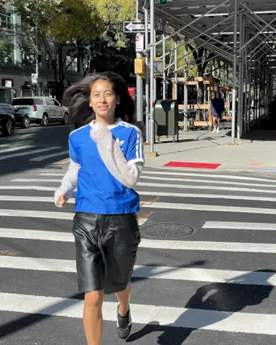 Michelle wearing an Adidas jersey, leather Bermuda shorts, and Adidas Taekwondo shoes on a crosswalk in New York City.