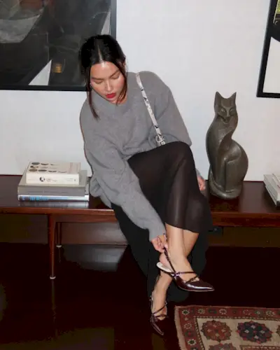 Fashion person Mimi Nguyen wears a brown shoe outfit. She pairs her brown strappy kitten heel shoes with a grey jumper, snake print bag and sheer skirt in a recent image taken from her Instagram.