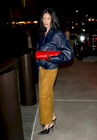 Meredith wears a navy leather jacket, red bag, and suede pencil skirt.