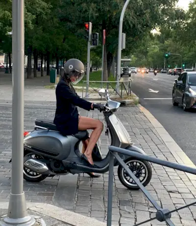 Woman wearing black blazer and black pumps, sitting on motorcycle and wearing helmet.