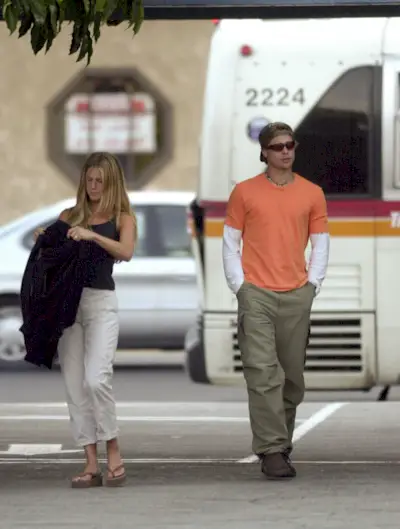Jennifer Aniston wears a pair of cream trousers with a black vest top in the 90s