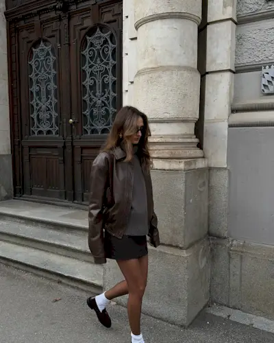 woman wears bomber and skirt and loafer
