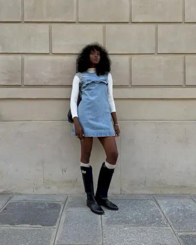 Woman wears denim mini dress, cream roll neck and knee high black boots