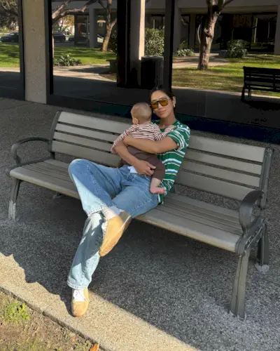 Fashion influencer @aimeesong sitting on a bench holding her baby, wearing a chic spring outfit with on-trend sneakers.