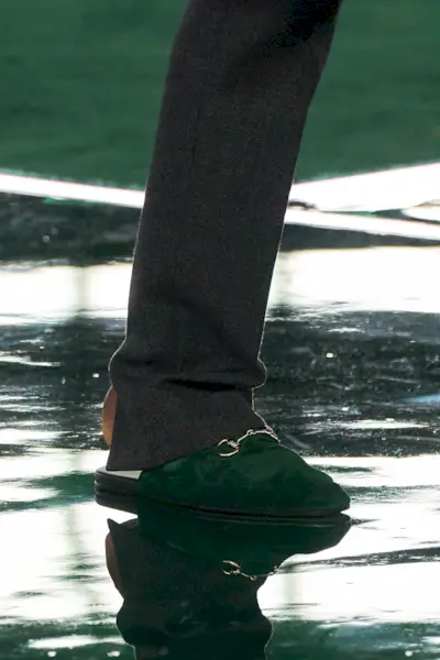 A model at Gucci's F/W 25 show wearing gray pants and green flat mules.