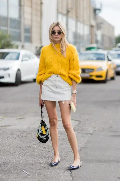 Woman wearing a yellow sweater with a white denim miniskirt and slingback flats.
