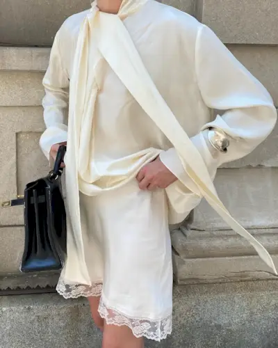 Christie Tyler wearing a cream silk scarf blouse with a lace-trim matching skirt.