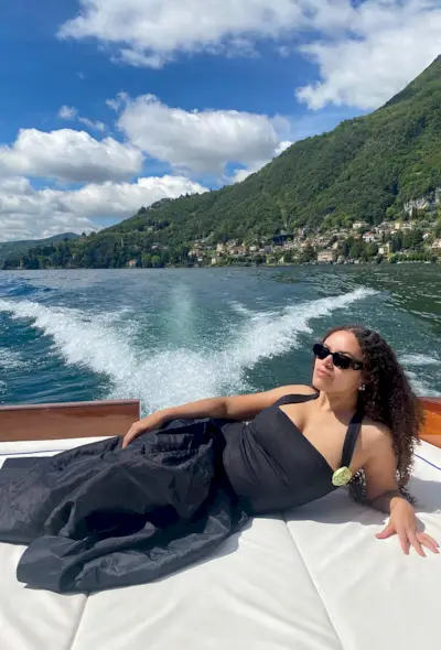 a photo showing what to wear on a boat with a woman wearing black sunglasses, silver hoops, a black halter top, and a black a-line full skirt
