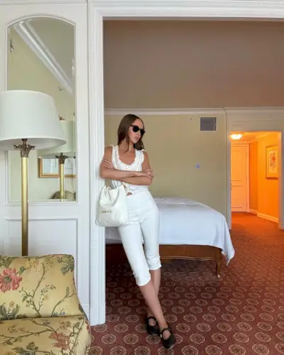 Fashion person Makenna wears the white lace camisole trend, white capri trousers, buckled ballet flats and carries a white Chanel hobo bag. She is stood in a hotel bedroom and is lent against a wall in a image taken from her Instagram recently.