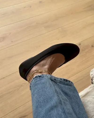 Woman wearing chocolate brown ballet flats with anklets and straight-leg denim jeans.