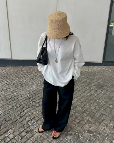 Debora Rosa wearing a straw hat, white T-shirt, and black drawstring pants with red flip flops.