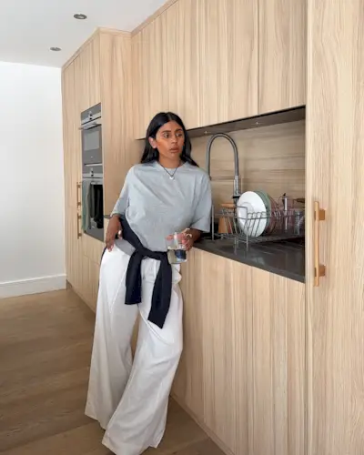 Monikh wearing a gray T-shirt, black sweater, and white linen drawstring pants.