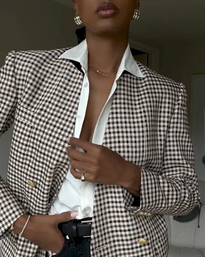 Model Jasmine Tookes wears checkered blazer, white button down, and black jeans while posing in tennis bracelet.
