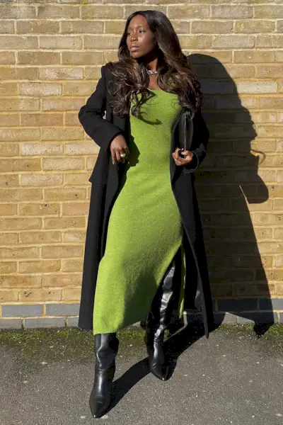 a photo of a sweater dress outfit with a woman wearing a bright green midi knit dress with a black long wool coat with black over-the-knee boots