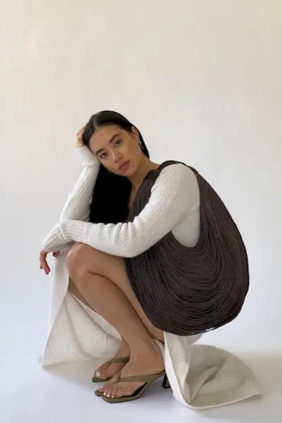 a photo of a sweater dress outfit with a woman wearing a white knitted maxi dress with a brown hobo bag and olive green thong heeled sandals