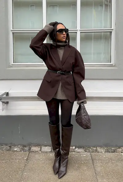 a photo of a sweater dress outfit with a woman wearing a brown mini turtleneck dress with a brown blazer, brown belt, brown tights, brown knee-high boots, and a brown handbag