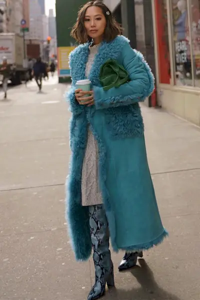 a photo of a sweater dress outfit with a woman wearing a blue shearling coat over a gray sweater dress with blue snakeskin knee high boots