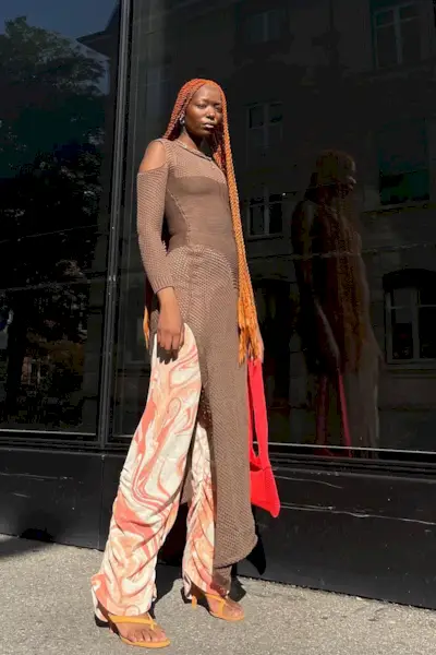 a photo of a sweater dress outfit with a woman wearing a brown sweaterdress over printed orange and white pants styled with orange sandals