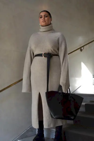 a photo of a sweater dress outfit with a woman wearing a turtleneck sweaterdress with a black belt and black tote bag and black sock boots