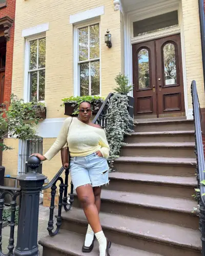 @aniyahmorinia wearing pale yellow sweater, denim shorts, and white loafers on a Brooklyn stoop