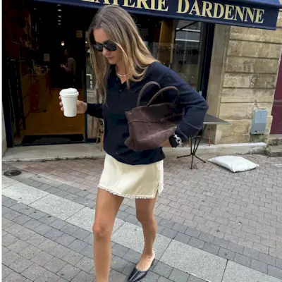 Anne-Laure Mais wearing a navy polo with a butter yellow skirt and a brown suede bag.