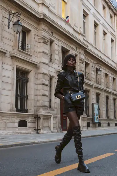 a photo of a thigh-high boots outfit shown on a woman walking down the street wearing a black leather top styled with matching shorts and black tall boots