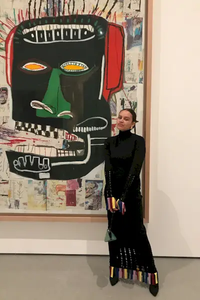 a photo of a thigh-high boots outfit shown on a woman in an art gallery wearing a black turtleneck sweater dress with black thigh-high boots and a clutch bag