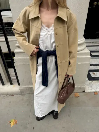 An image of @chloekathbutler wearing a cotton maxi dress with a trench coat, sweater and loafers