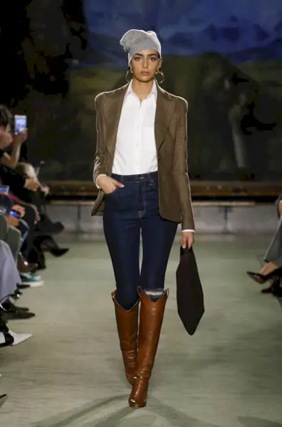 best riding boots shown in a photo from Brandon Maxwell's fall 2020 runway show with a model wearing a brown blazer over a white button-down shirt with skinny jeans and brown riding boots
