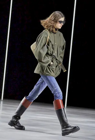 best riding boots shown in a photo from Celine's fall 2022 runway show with a model wearing a green barn jacket with skinny jeans and riding boots